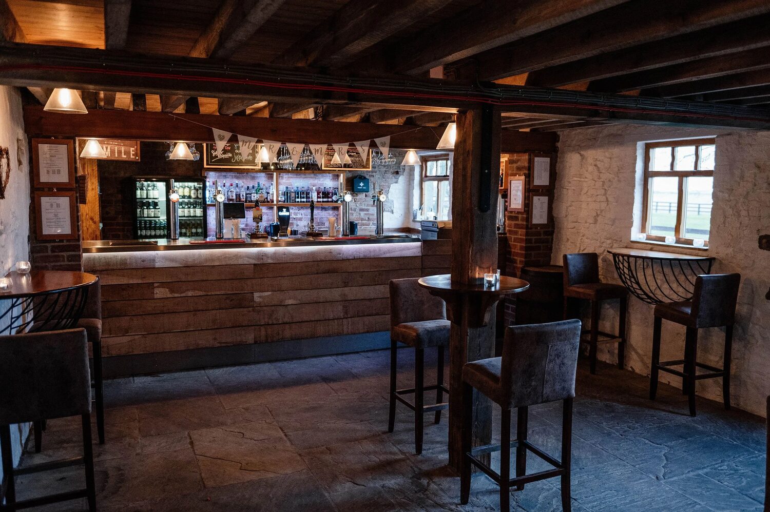 The fully stocked bar with backlit bottles, leather stools and exposed beams
